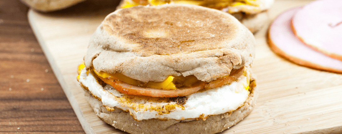 An egg and ham breakfast sandwich sitting on a cutting board.