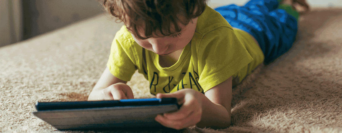 A young boy laying on top of his bed with a tablet.
