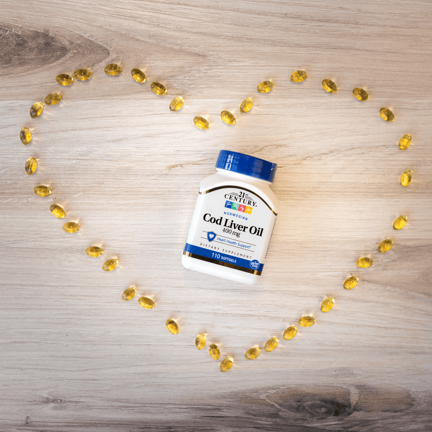 A bottle of 21st Century Norwegian Cod Liver Oil 400 mg softgels laying on a wood floor surrounded by softgels in the shape of a heart.