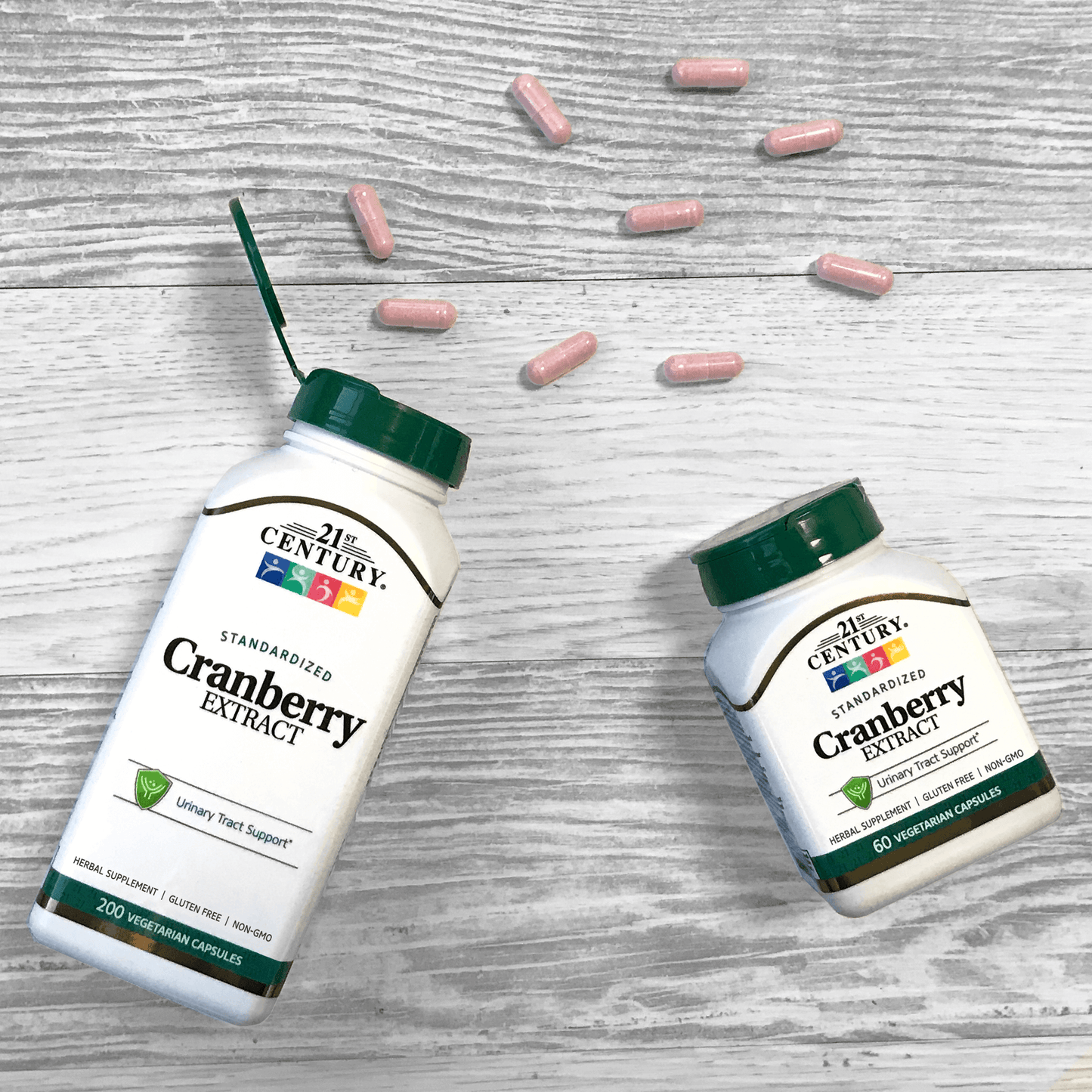 Two bottles of 21st Century Cranberry Extract vegetarian capsules laying on a wood floor with capsules coming out of the top.