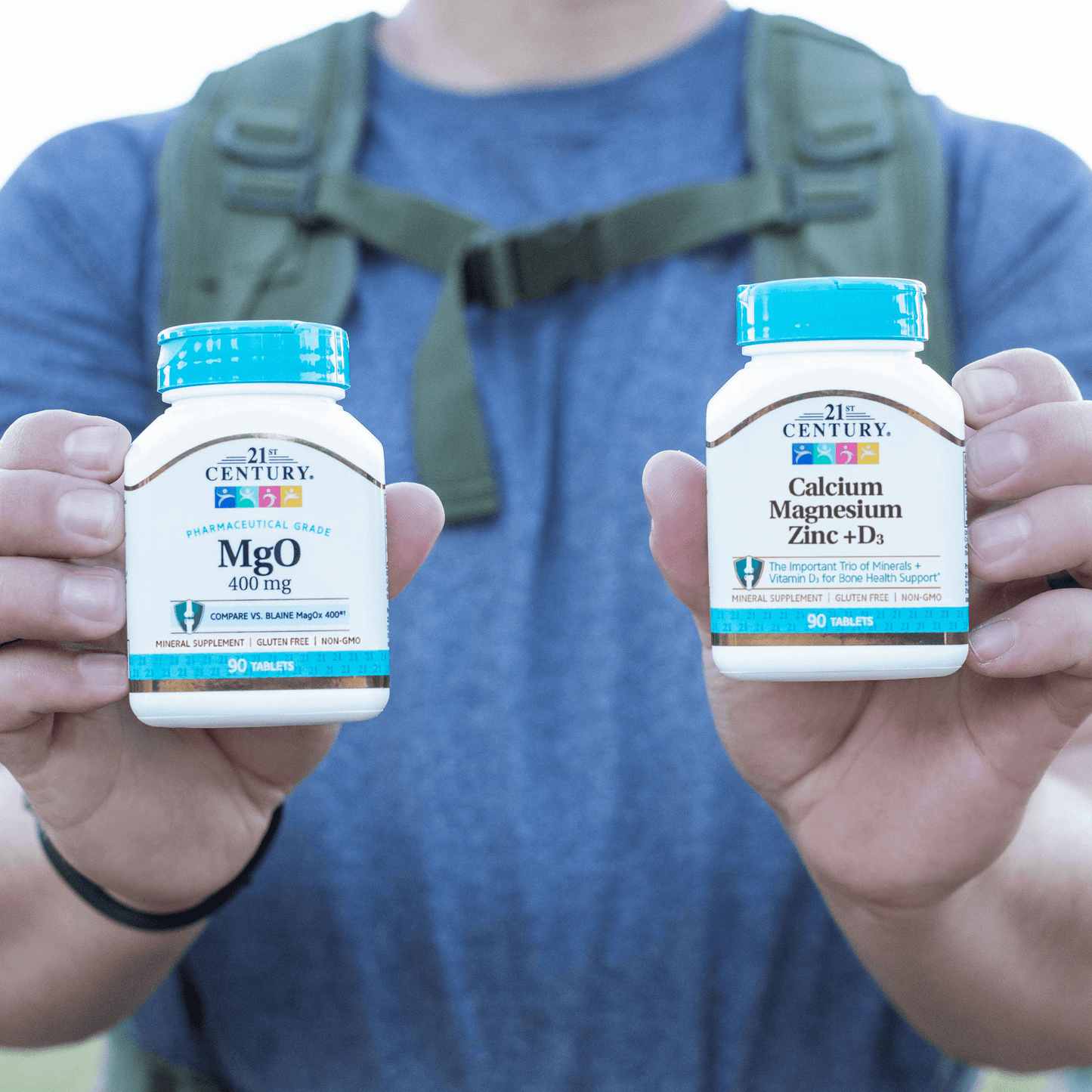 A man on a hiking rail holding a bottle of 21st Century Calcium Magnesium Zinc plus D3 tablets and a bottle of MgO 400 mg tablets.