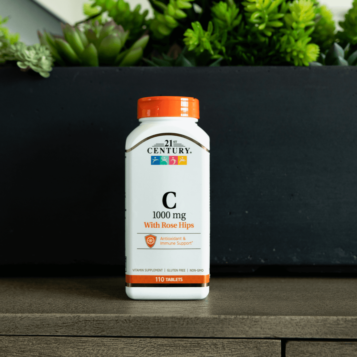 A bottle of 21st Century Vitamin C 1000 mg with Rose Hips tablets with a potted plant in the background.