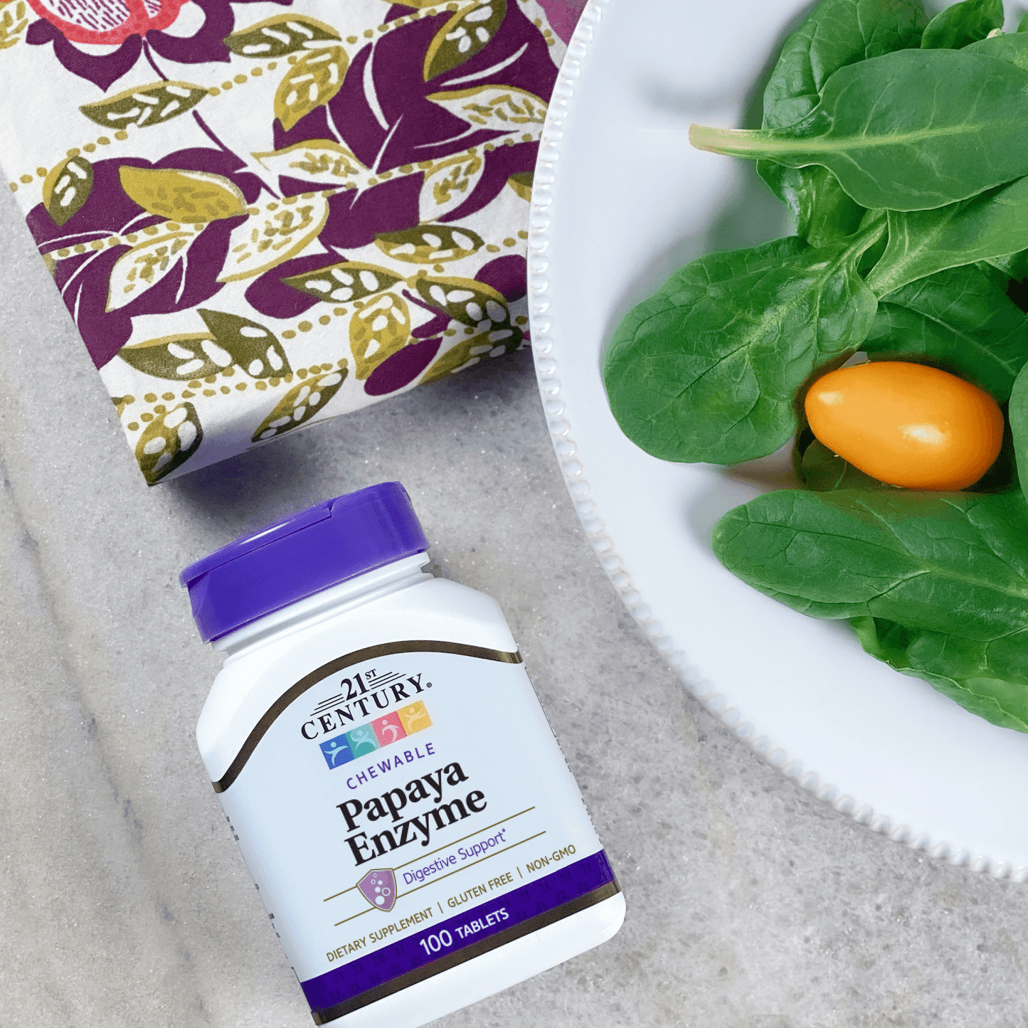A bottle of 21st Century Papaya Enzyme chewable tablets next to a dinner plate of salad and a dinner napkin.