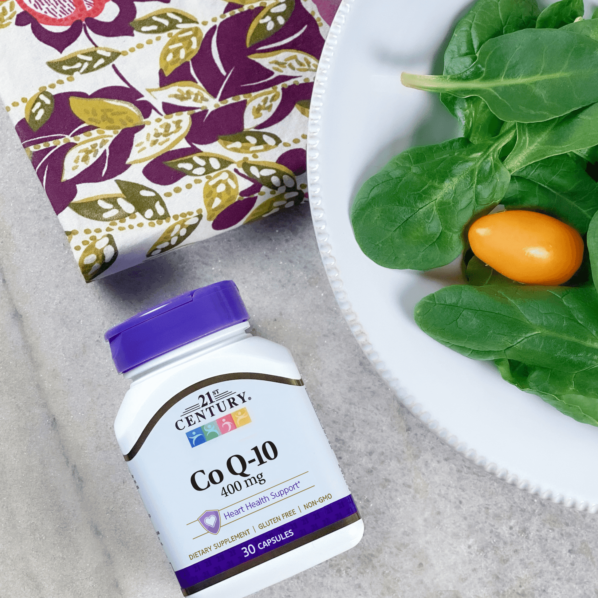 A bottle of 21st Century Co Q-10 400 mg capsules laying on a table with a dinner plate of salad and napkin.