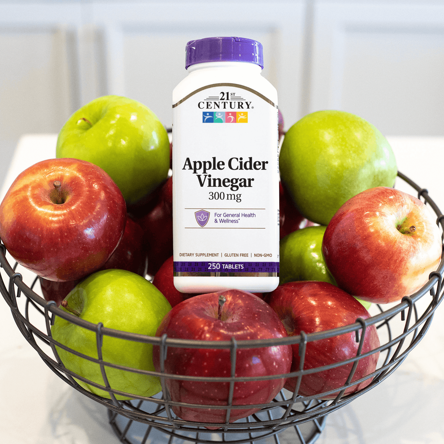 A bottle of 21st Century Apple Cider Vinegar 300 mg tablets sitting in a basket of green and red apples.