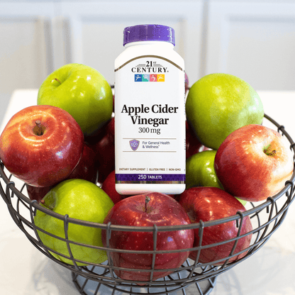 A bottle of 21st Century Apple Cider Vinegar 300 mg tablets sitting in a basket of green and red apples.