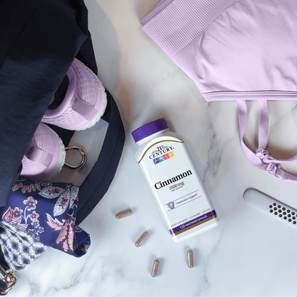 A bottle of 21st Century Cinnamon 1000 mg vegetarian capsules next to sports bra, running shoes, and a rolled up yoga mat in a gym bag.