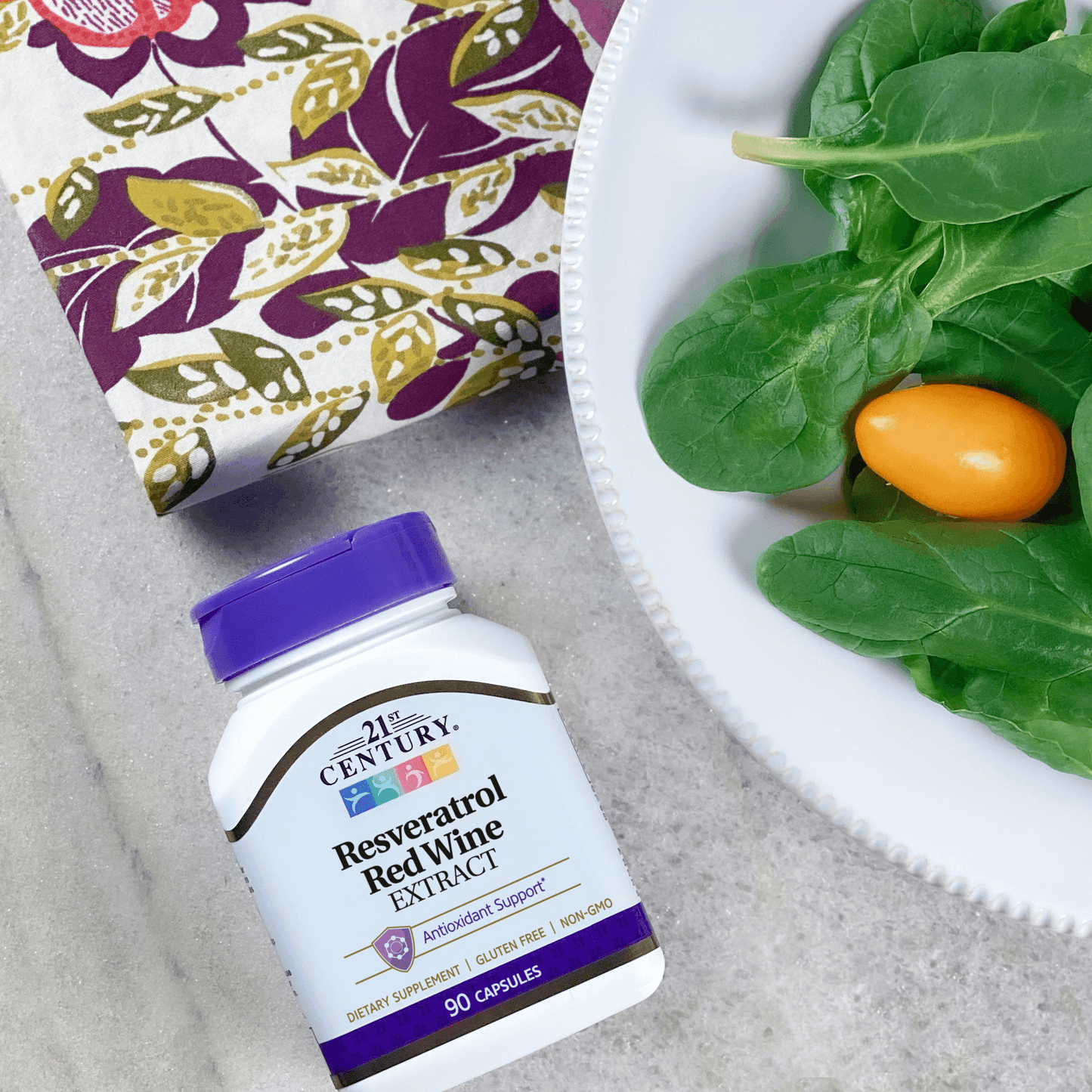 A bottle of 21st Century Resveratrol Red Wine Extract on table text to a dinner plate of salad and a napkin.