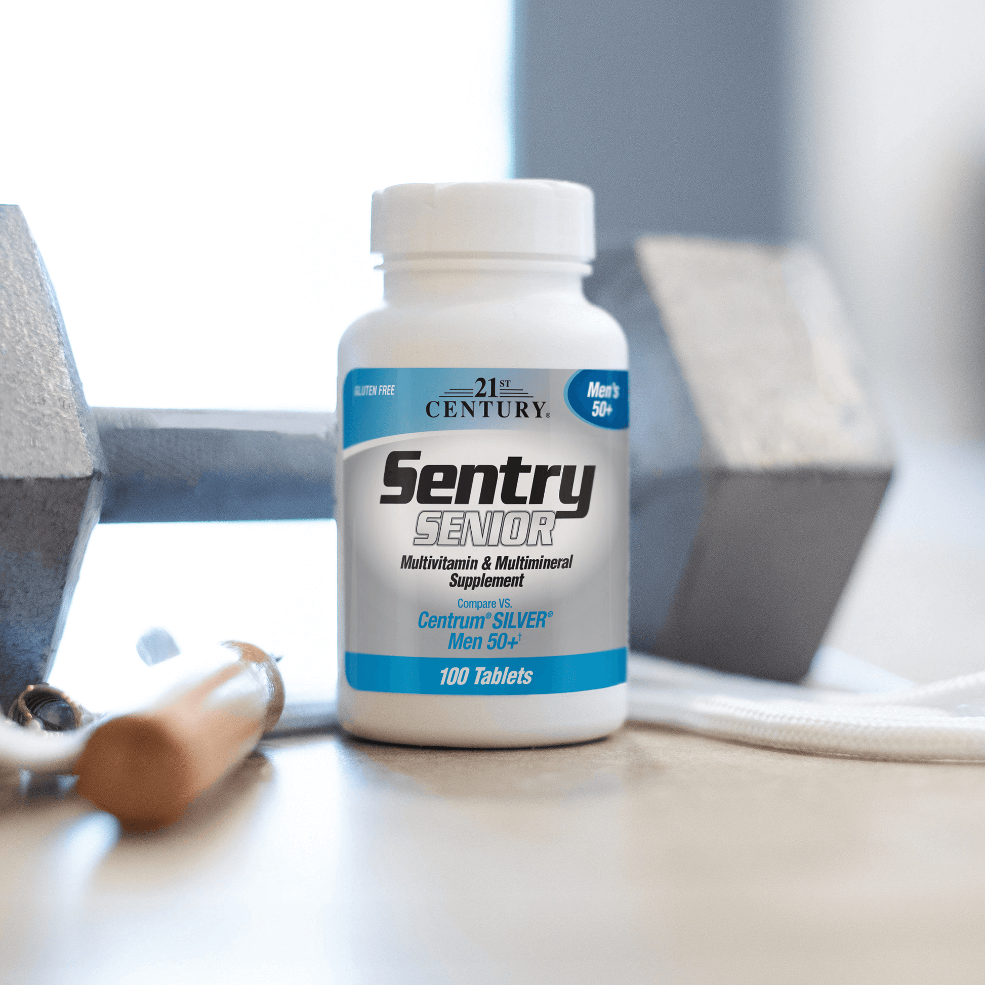 A bottle of 21st Century Sentry Senior Men's 50+ Multivitamin and Multimineral tablets on a table with a dumbbell in the background.