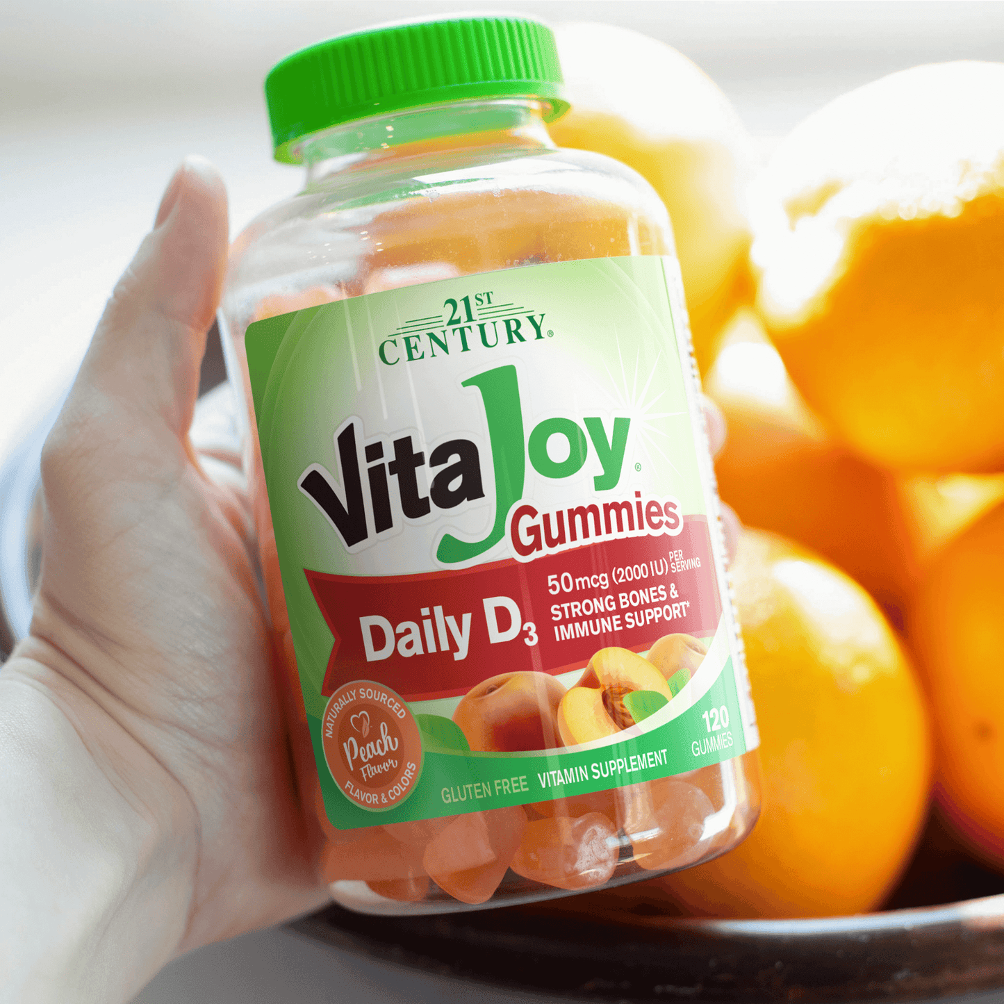 A woman holding a bottle of A bottle of 21st Century VitaJoy Daily D3 50 mcg gummies and peaches in the background.