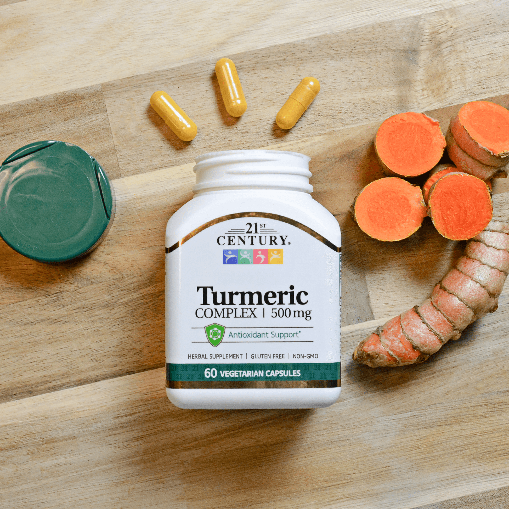 A bottle of 21st Century Turmeric 500 mg Complex vegetarian capsules laying on a wood background with capsules coming our of the top and turmeric root to the right.