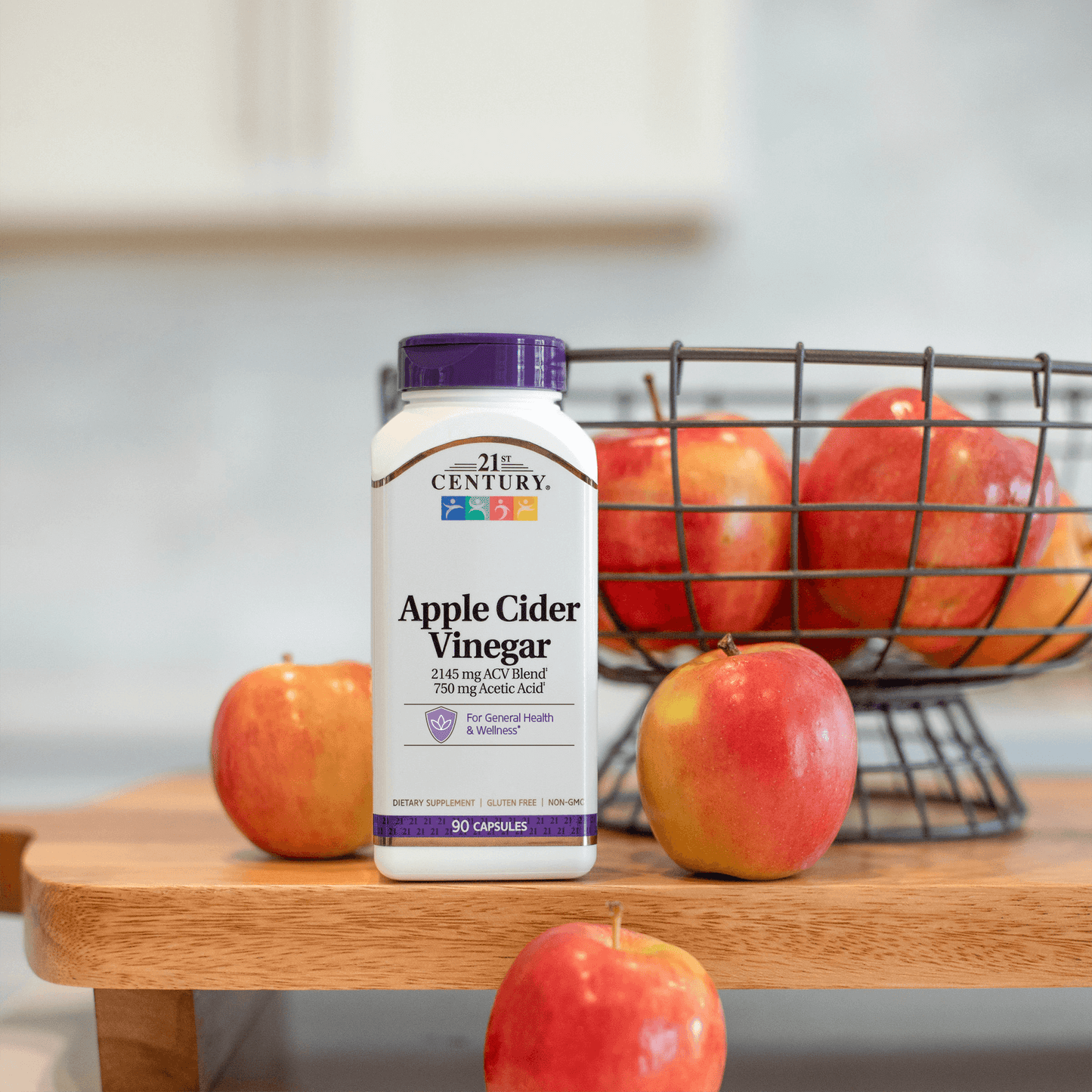 Bottle of 21st Century Apple Cider Vinegar with a basket of apples on a wooden surface.
