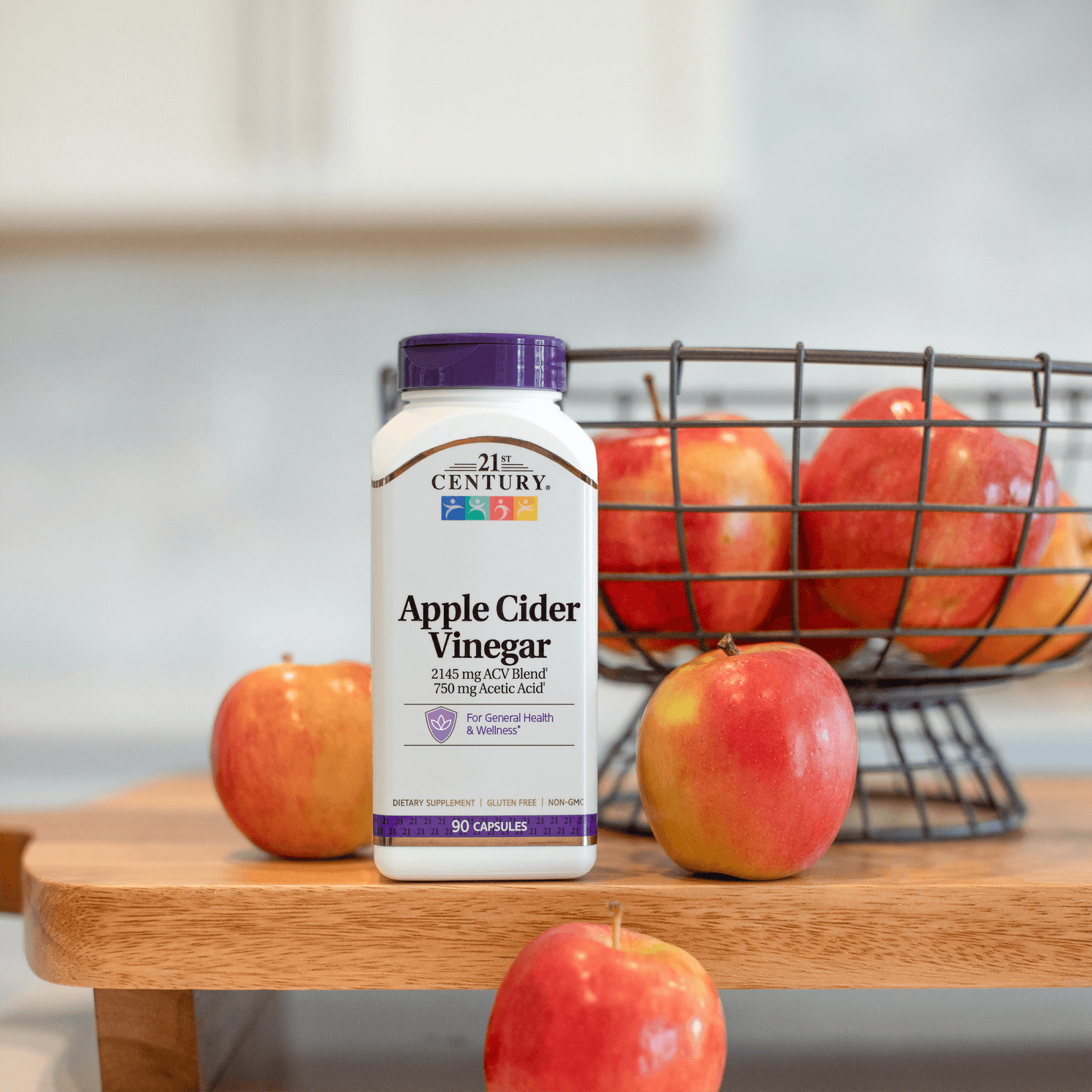 Bottle of 21st Century Apple Cider Vinegar with a basket of apples on a wooden surface.