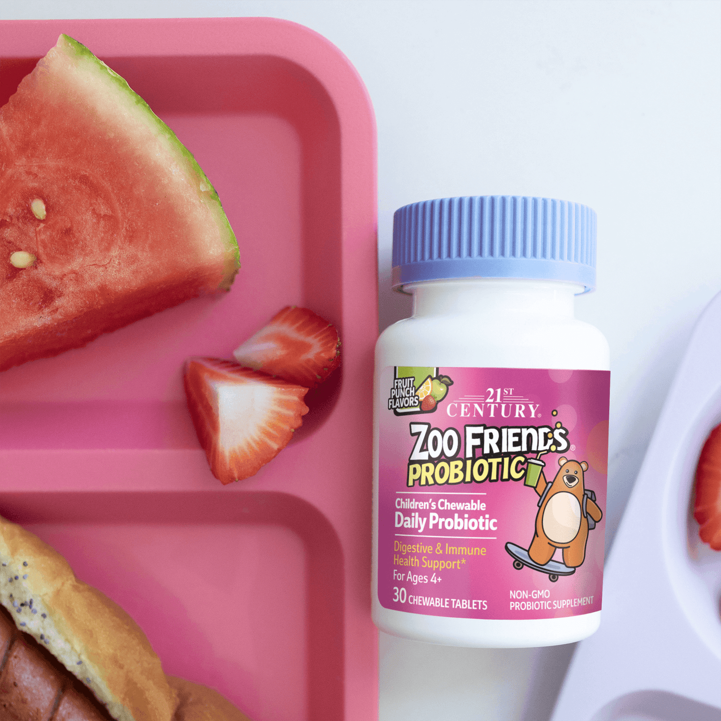 A bottle of 21st Century Zoo Friends Probiotic chewable tablets next to a child's plate with watermelon, strawberries and hotdogs.