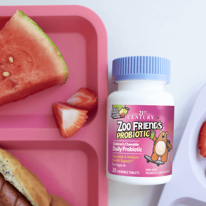 A bottle of 21st Century Zoo Friends Probiotic chewable tablets next to a child's plate with watermelon, strawberries and hotdogs.
