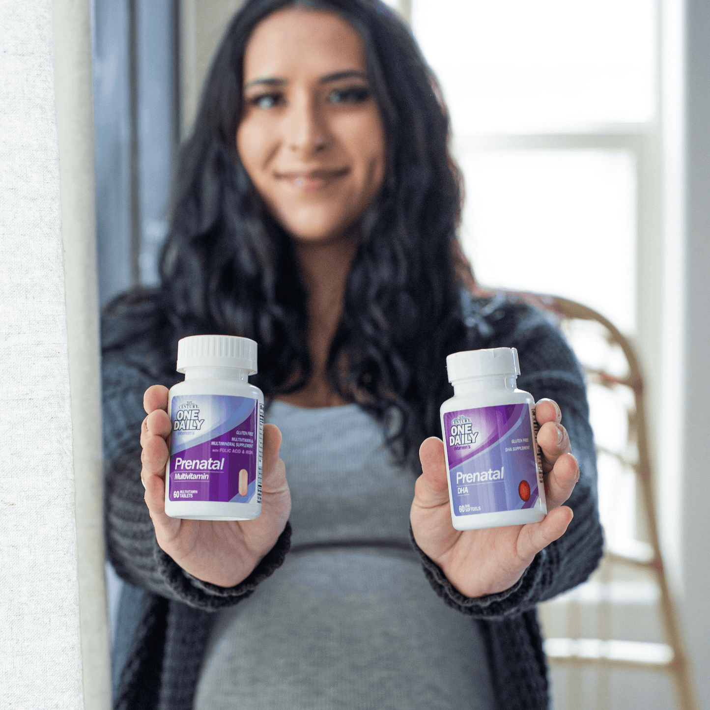 A pregnant woman holding a bottle of 21st Century One Daily Prenatal Multivitamin Plus DHA tablets and softgels.