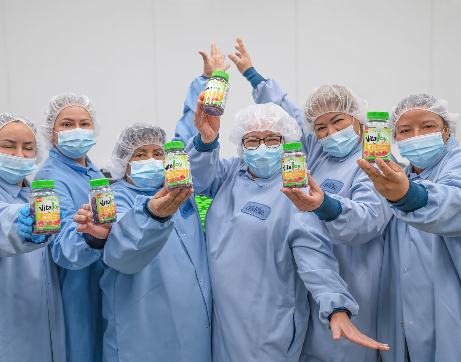 Group of people in blue protective suits holding colorful bottles against a white background