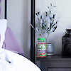 A bottle of 21st Century Melatonin 5 mg gummies on a side table with a faux plant next to a bed in a bedroom.