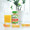A bottle of 21st Century VitaJoy Daily C 250 mg gummies next to a glass of orange juice with vitamin c gummies in the foreground.