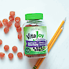 A bottle of 21st Century VitaJoy Sambucus Elderberry 100 mg per serving with vitamin c and zinc gummies laying on table with elderberry gummies and two pencils.