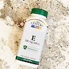 A bottle of 21st Century Vitamin E 180 mg softgels laying on a tile surface.