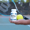 A man holding a bottle of 21st Century Sentry Mens Multivitamin and Multimineral tablets and tennis ball, with a tennis rack, on a tennis court.