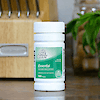 A bottle of 21st Century One Daily Essential multivitamin and mineral supplement tablets on a kitchen counter with a butcher block in the background.