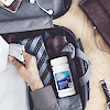 A bottle of 21st Century One Daily Men's Health Multivitamin and Multimineral tablets in a suitcase with a tie and a man placing a folded work shirt inside.
