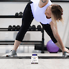 A bottle of 21st Century Lycopene 25 mg tablets with a woman stretching on a yoga mat in the background in front of a dumbbell rack and medicine ball.
