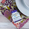 A bottle of 21st Century Alpha Lipoic Acid 200 mg capsules on a dinner napkin next to a dinner plate.