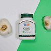 A bottle of 21st Century Garlic Extract enteric coated tablets laying on a background with two garlic cloves.