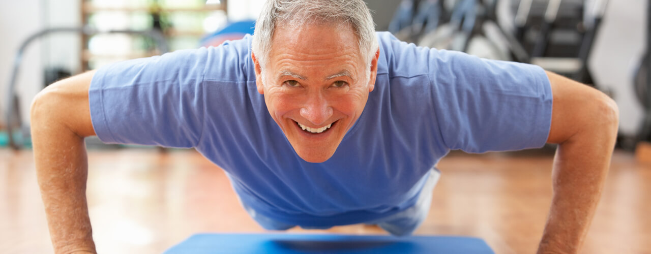 An older man in a gym doing push ups.