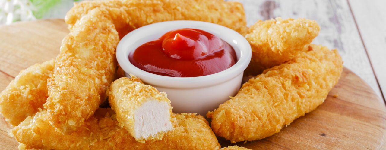 A delicious stack of chicken tenders next to a cup of ketchup.