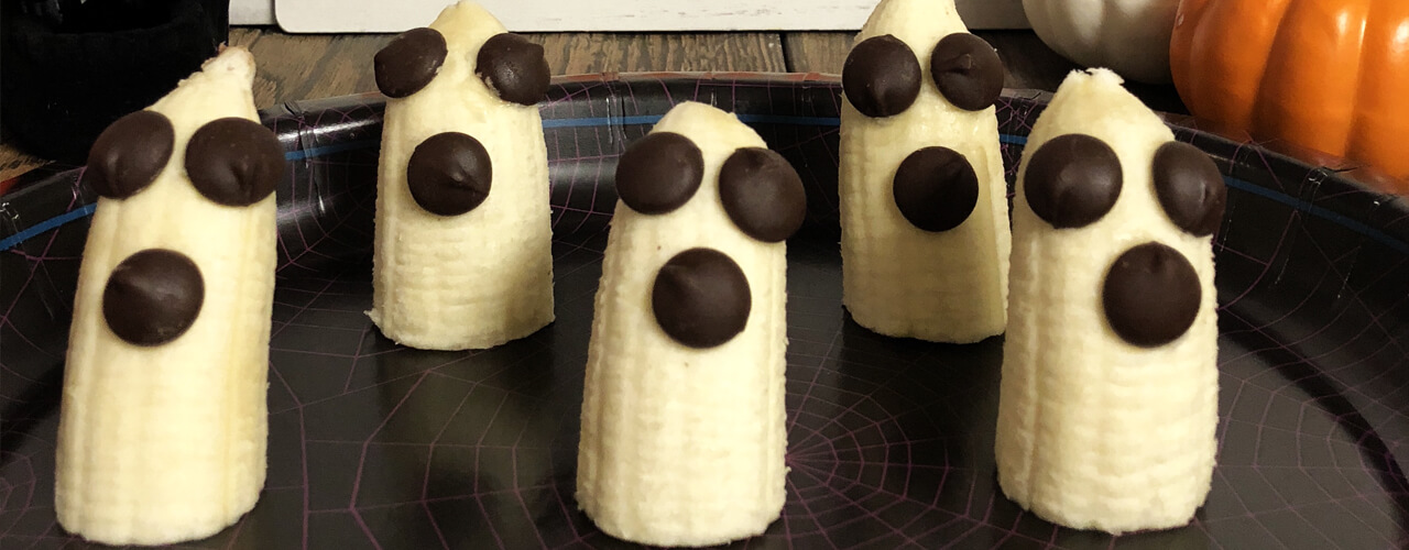 Bananas sliced in half and standing on plate with chocolate chips for eyes and mouth.