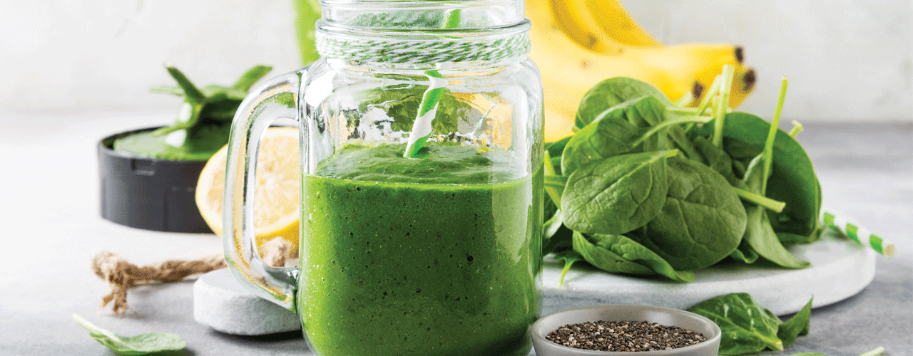 A St. Patrick's Day green smoothie in a glass next to bananas and kale.