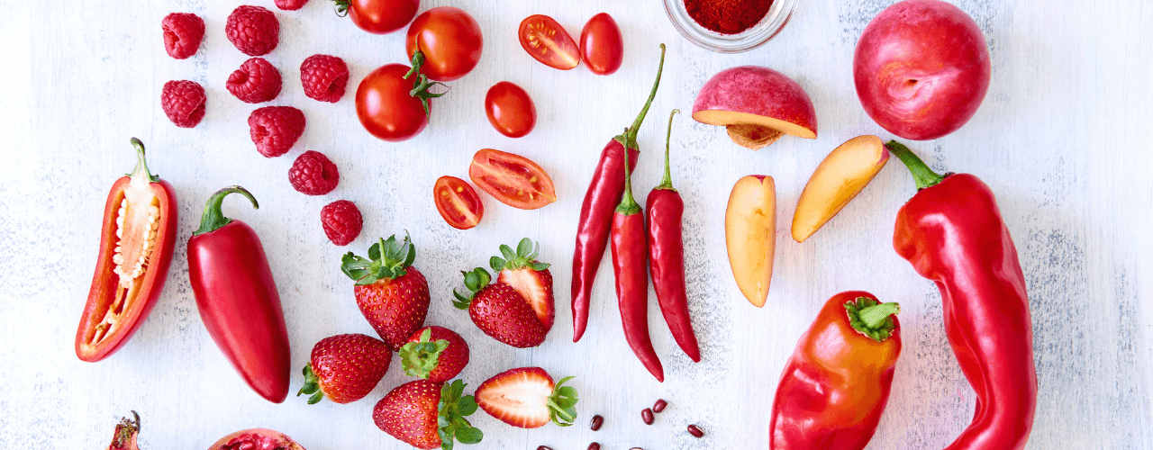 Red colored summer produce like peppers, chilis, tomatoes, pomegranate, raspberries and strawberries.
