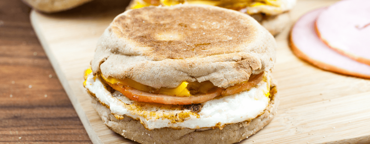An egg and ham breakfast sandwich sitting on a cutting board.