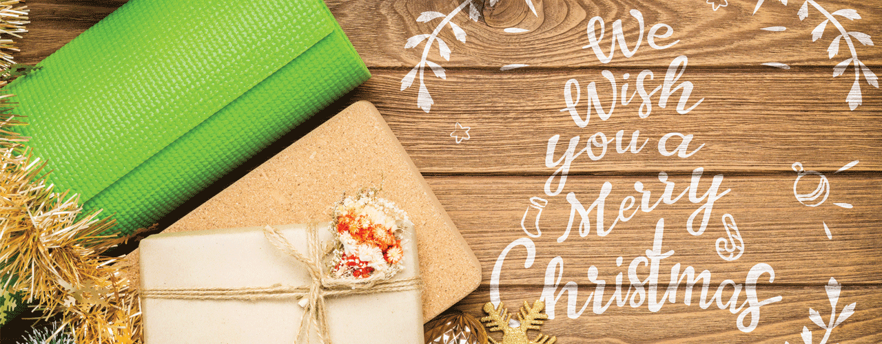 Wrapped gifts, a yoga mat and Christmas bulbs next to the holiday greeting, We Wish You a Merry Christmas. 