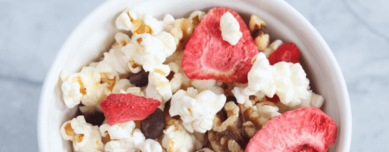 Top view of a bowl filled with nuts, berries and popcorn.