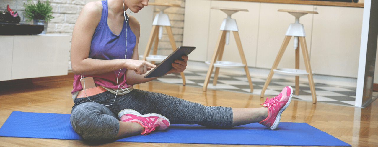 Young woman sitting on yoga mat in looking at an iPad.