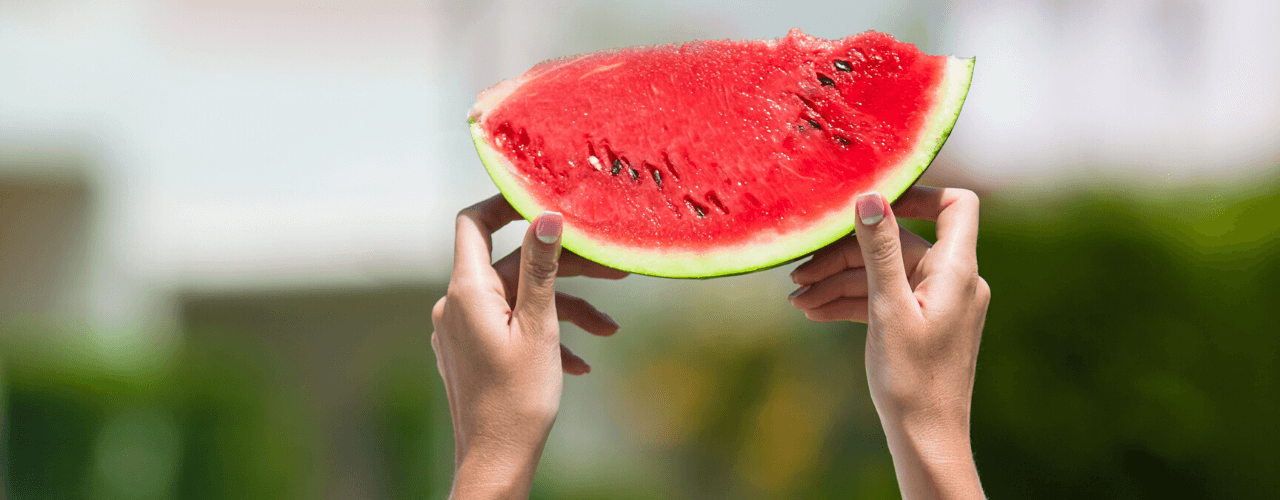 Two hands holding up a quarter slice of watermelon.