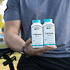 A muscular man sitting on a bike holding two bottles of 21st Century Calcium 1000 mg Plus D3 20 mcg tablets.