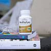 A bottle of 21st Century Healthy Eyes Extra with Lutein, Zinc and Vitamin B tablets on a stack of books with reading glasses on the left.