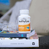 A bottle of 21st Century Healthy Eyes Lutein and Zeaxanthin capsules on a stack of books with reading glasses on the left.