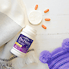 A bottle of 21st Century PreNatal tablets laying on a baby blanket and tablets coming out of the top with a teddy bear in the corner.