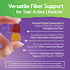 A woman's hand holding two fiber gummies between her finger and the claims versatile fiber support for your active lifestyle, morning routine supplement to support digestive wellness throughout the day, complement to a balanced diet when fiber intake is insufficient, travel companion to support regularity when away from home, and part of a comprehensive wellness regimen for digestive health.